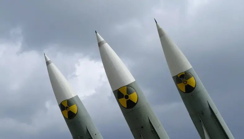 Three nuclear missiles pointed upward toward a cloudy sky. Each missile bears a radioactive hazard symbol. 